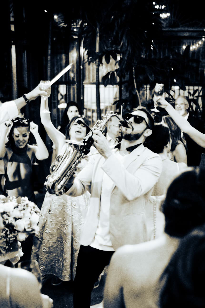 Bruno Daner tocando saxofone entre convidados que brindam em evento corporativo