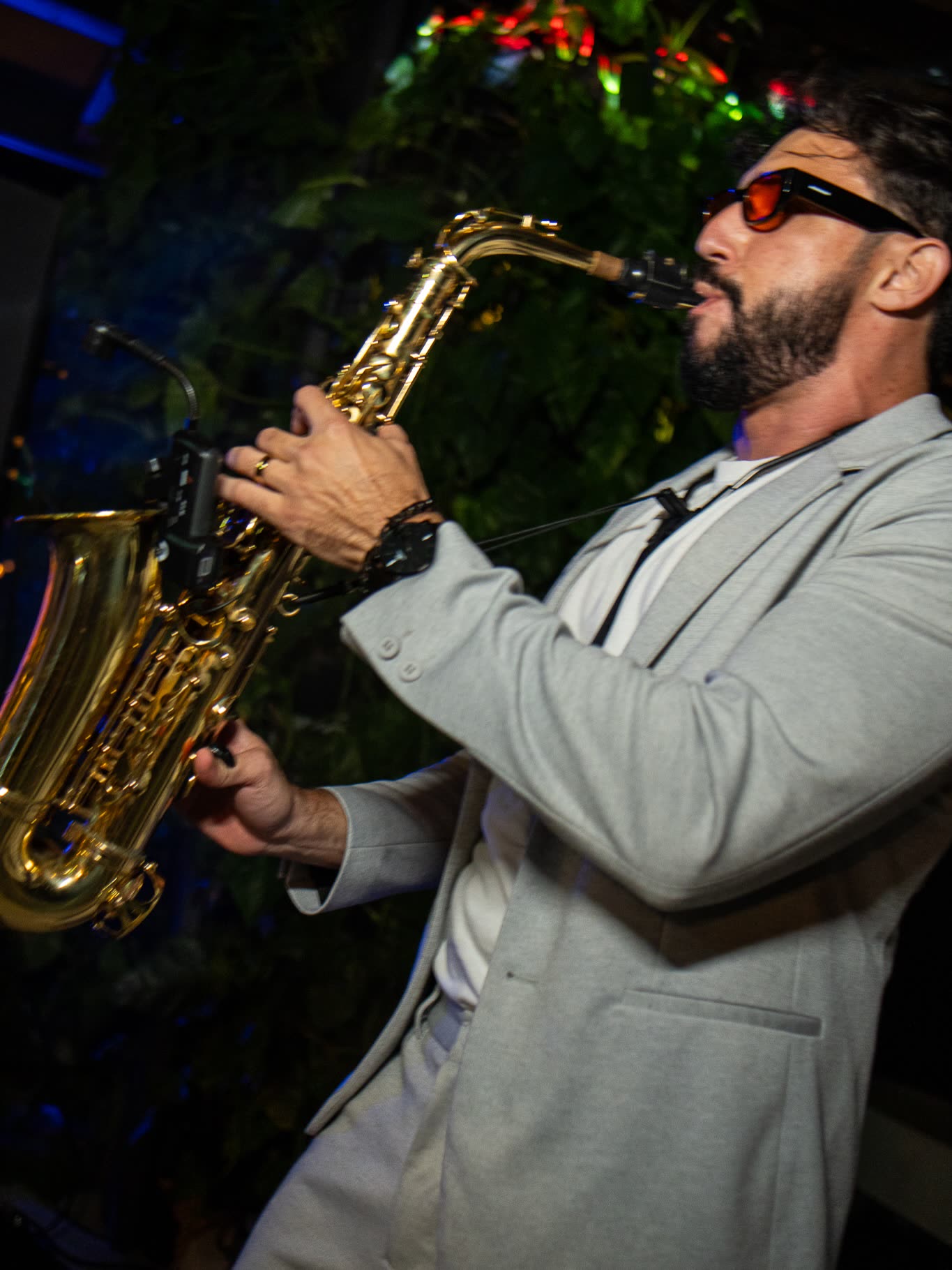 Bruno Daner de perfil tocando saxofone entre convidados